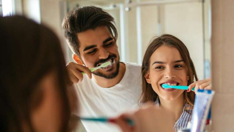 A couple brushing their teeth in the mirror