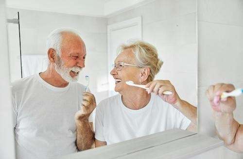 A laughing couple brushing their teeth together