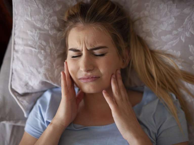 A woman with a toothache from teeth grinding in bed